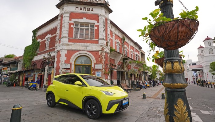 BYD Atto 1 warna kuning sedang melaju, perpaduan mobil listrik ringkas dengan baterai jarak jauh.